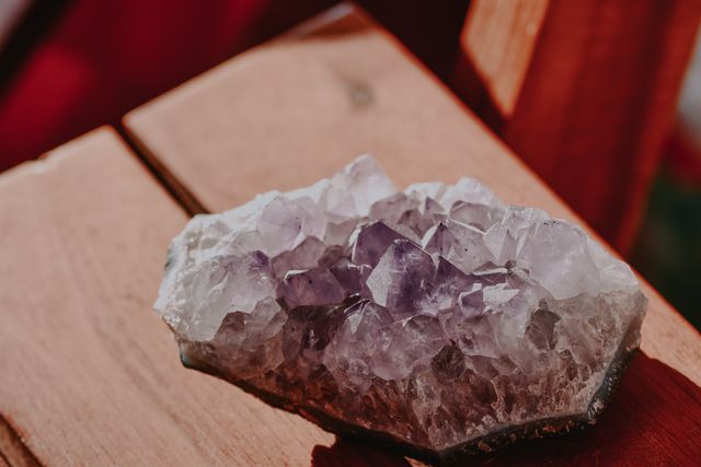 A raw amethyst crystal cluster resting on a warm wooden surface, highlighting the therapeutic amethyst stones used in biomat and infrared sauna wellness treatments.